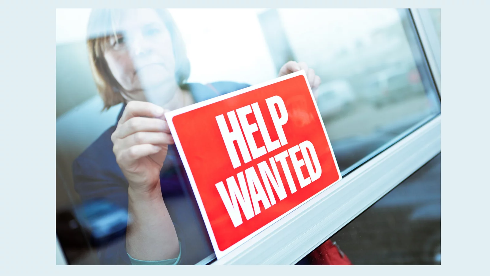 Woman placing Hel wanted sign in window