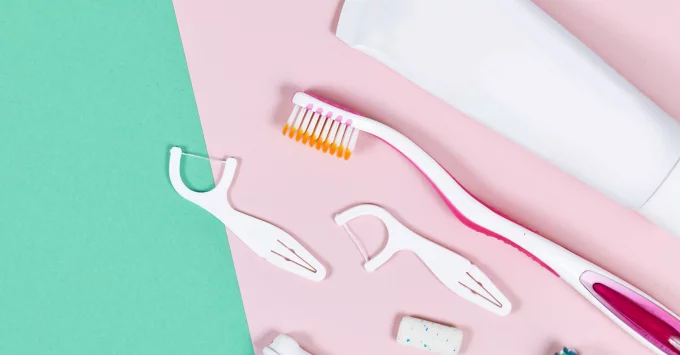 Toothbrush, toothpaste tube and flossers on a pink and green table cloth