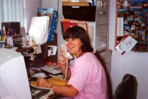 Becky in pink scrubs sitting at her crowded small desk