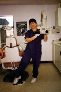 Becky in blue scrubs poses with the dental x-ray machine.