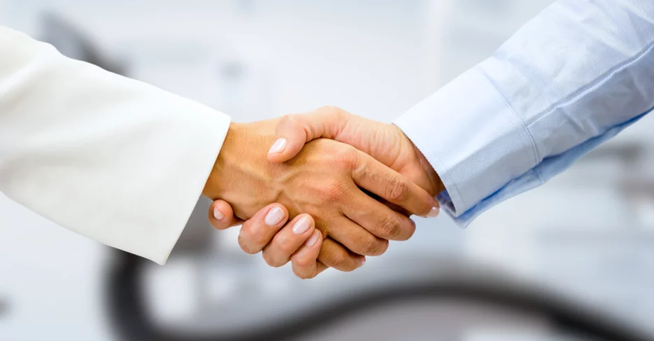 Two medical professionals seen from forearm to hand, shaking hands in a clinical environment