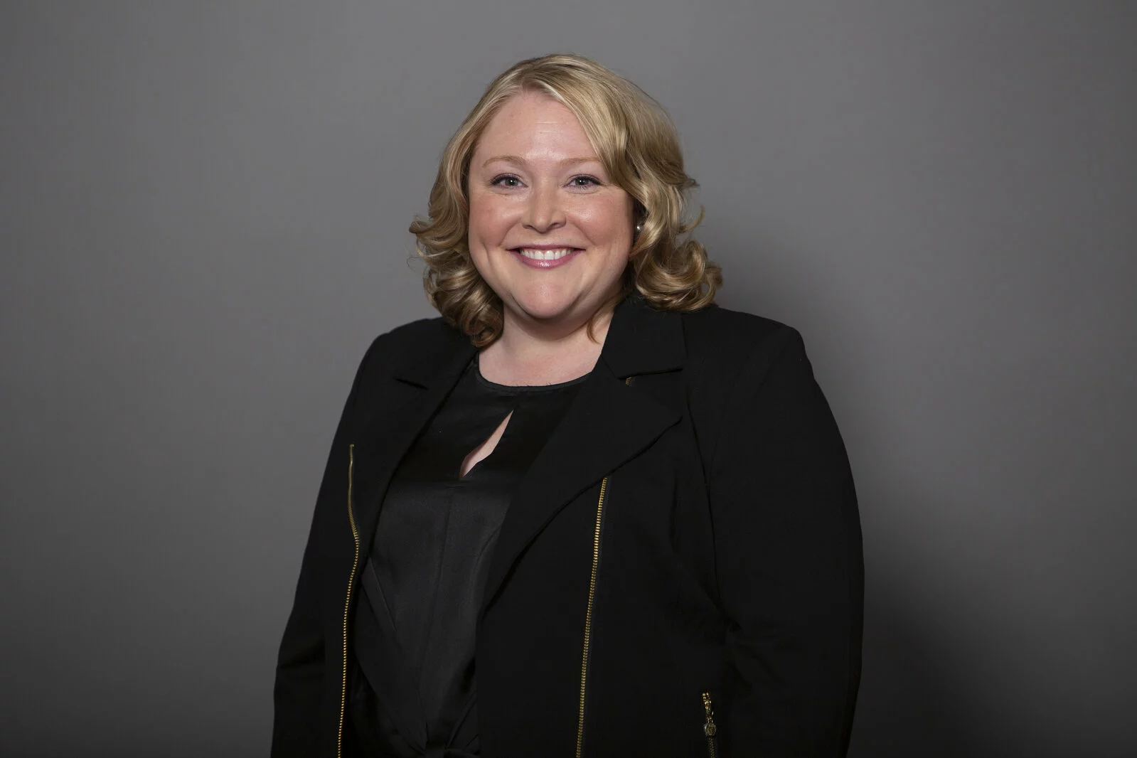 Headshot of Jessica August smiling wearing a black top and zippered black blazer