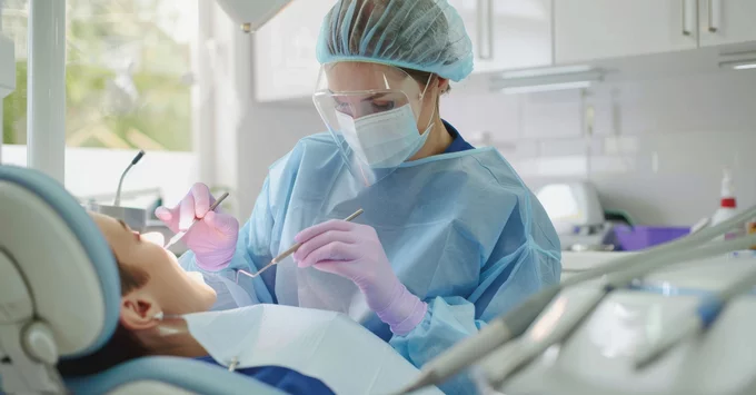 Hygienist in PPE including gloves holding instruments near patient in chair