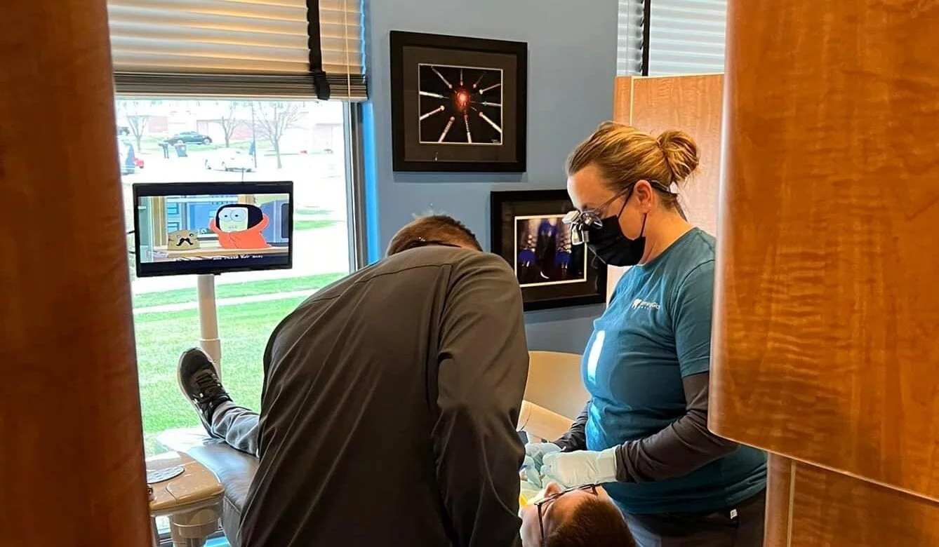 Dentist and dental hygienist lean over patient in operatory