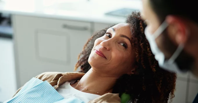 Female patient in dental chair with dental hygienist nearby in mask.