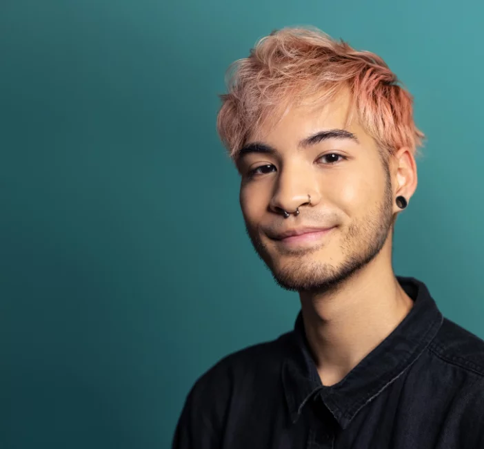 Young man in black shirt with coral dyed hair against green background