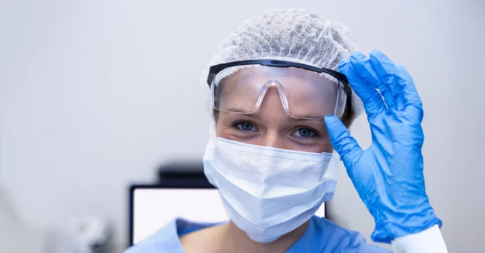 Female hygienist in mask, goggles, hair covering and gloves.