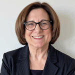 JoAnn Gurenlian smiling with glasses and black pinstriped jacket.