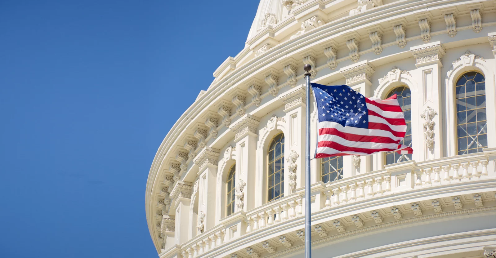 Cupola of the U.S. Capitol building in Washington DC with the U.S. flag flying in front.