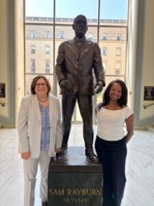 JoAnn Gurenlian and Katherine Williamson of ADHA stand on either side of a statue of Sam Rayburn at in the lobby of the Sam Rayburn Building in Washington DC