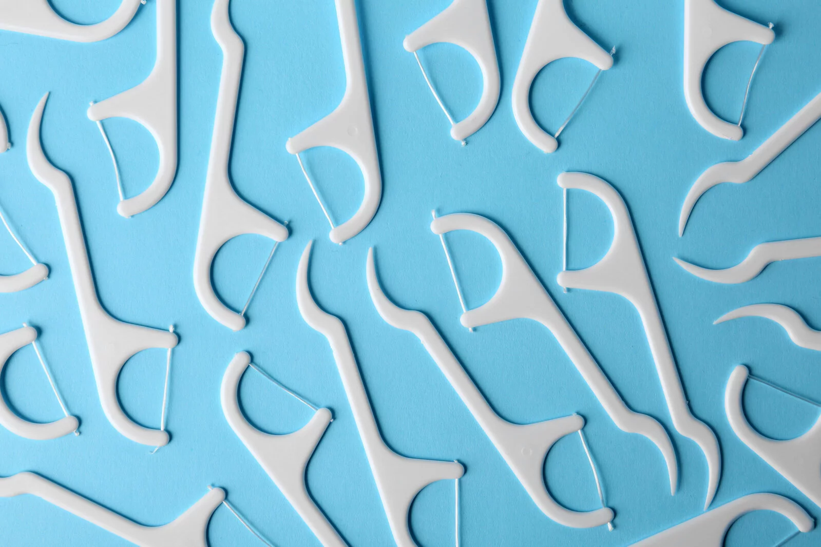 Top view of white floss picks arranged in all directions on a light blue background