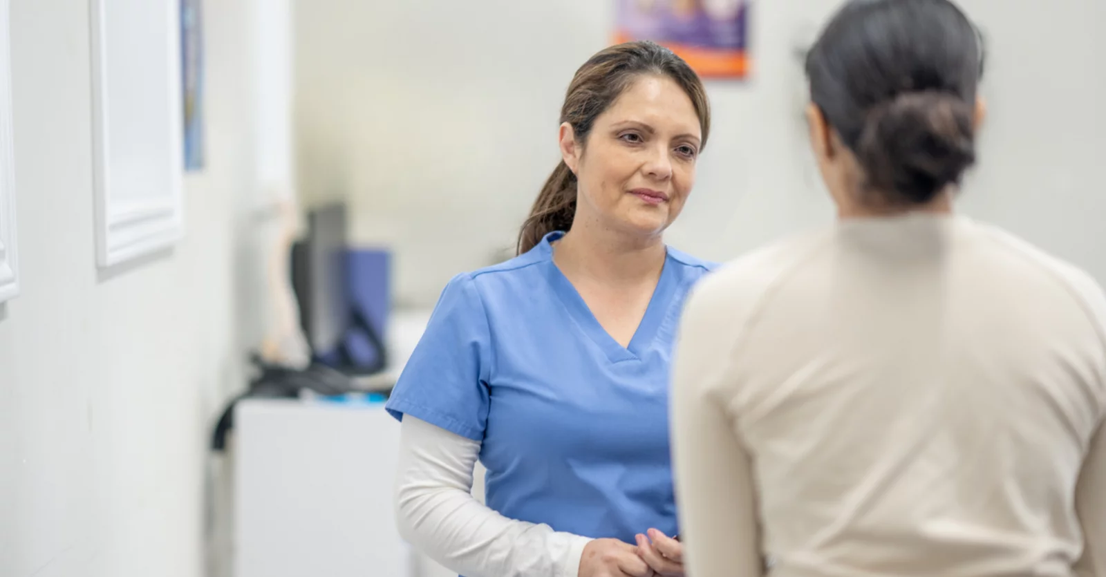 Clinician in scrubs sits opposite a patient and listens