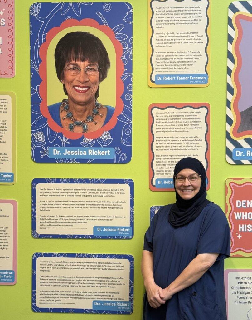 Woman in dark blue scrubs stands in front of a yellow wall decorates with quotes and large photos.