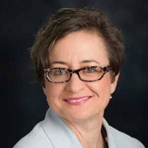 Headshot of Victoria Patruonova, grey suit, short brown hair, slim glasses