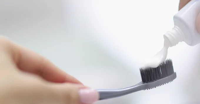 Hand squeezing white toothpaste onto grey tooth brush