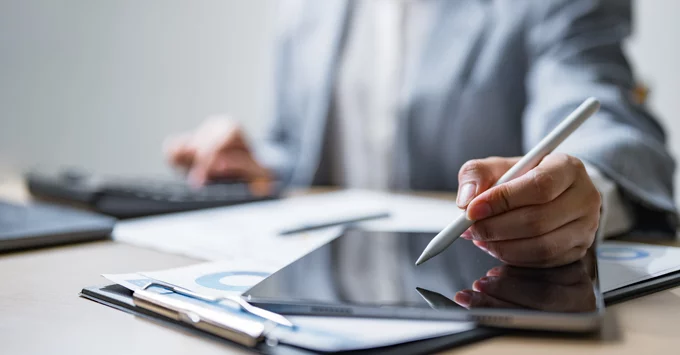 Female hands with i-pen in left hand, using iPad and calculator