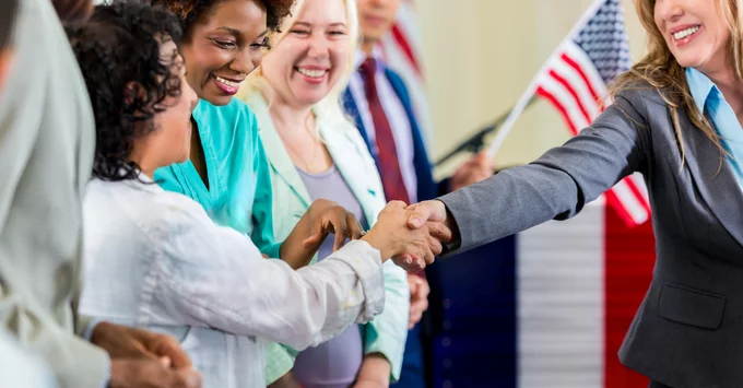 Group of women shaking hands with United States flag in background.