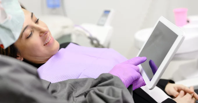 Hygienist with purple glove pointing at tablet screen with smiling patient