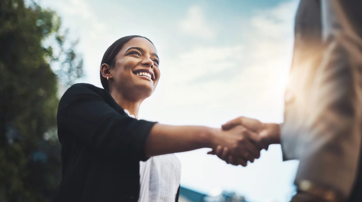 Young professional woman outdoors shaking hands with a person in a tan suit