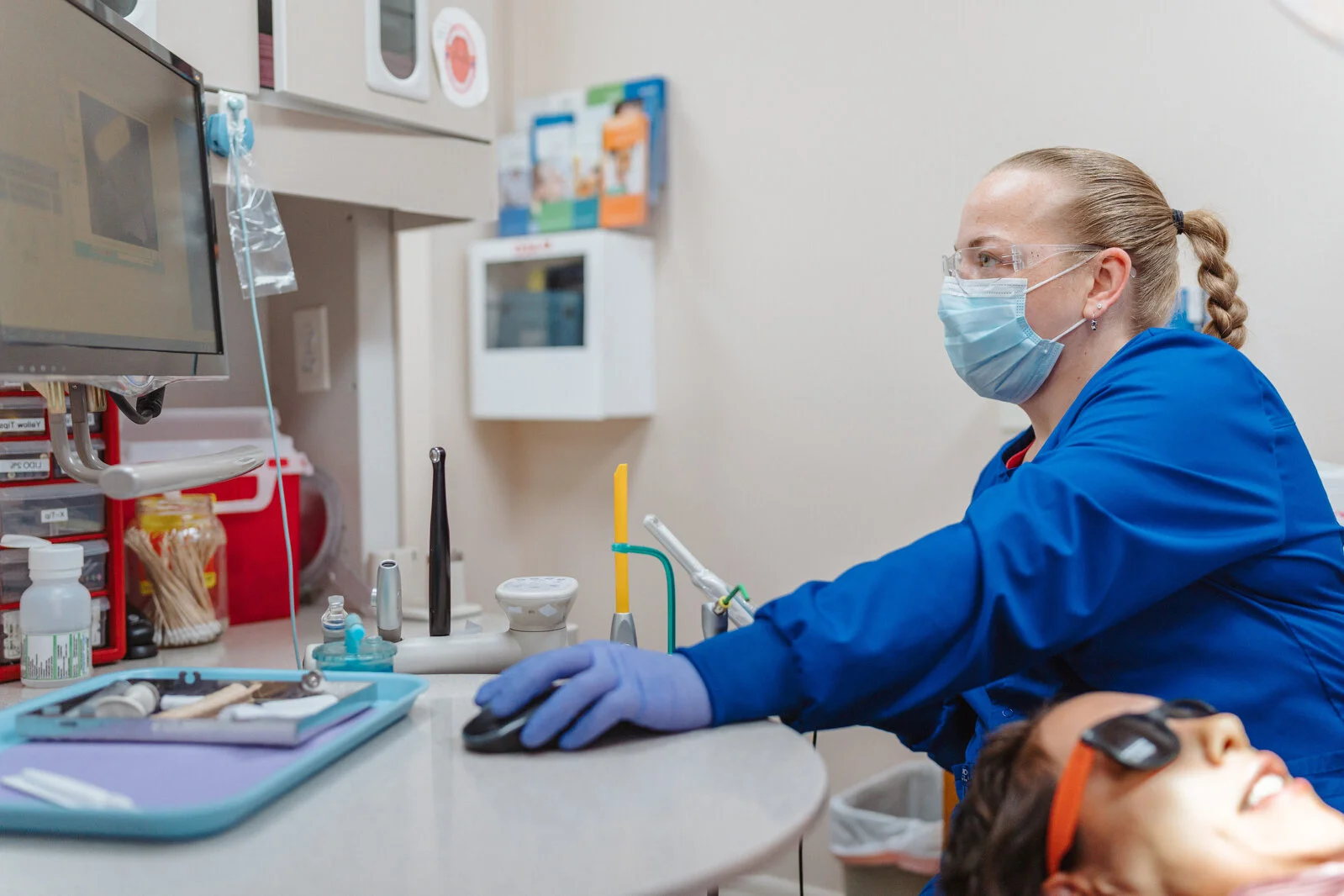 A female hygienist in ppe consulting a patient reviews dental images and the patient's medical chart on a computer in a dental operatory.