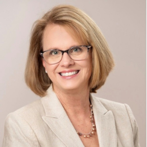 Marie Fluent,  DDS, CDICP, FACD, in cream jacket with necklace and glasses, smiling 