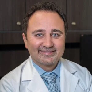 Kami Hoss, DDS smiling in lab coat and blue shirt and tie