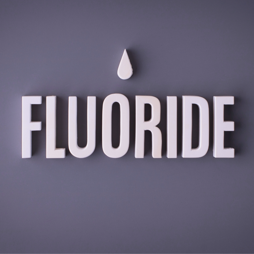 Fluoride. White block letters spelling fluoride beneath a single white droplet on a gray background.
