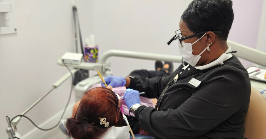 Jacy McKinney, RDH, wearing a mask and loupes, works on a reclined patient in a dental operatory.